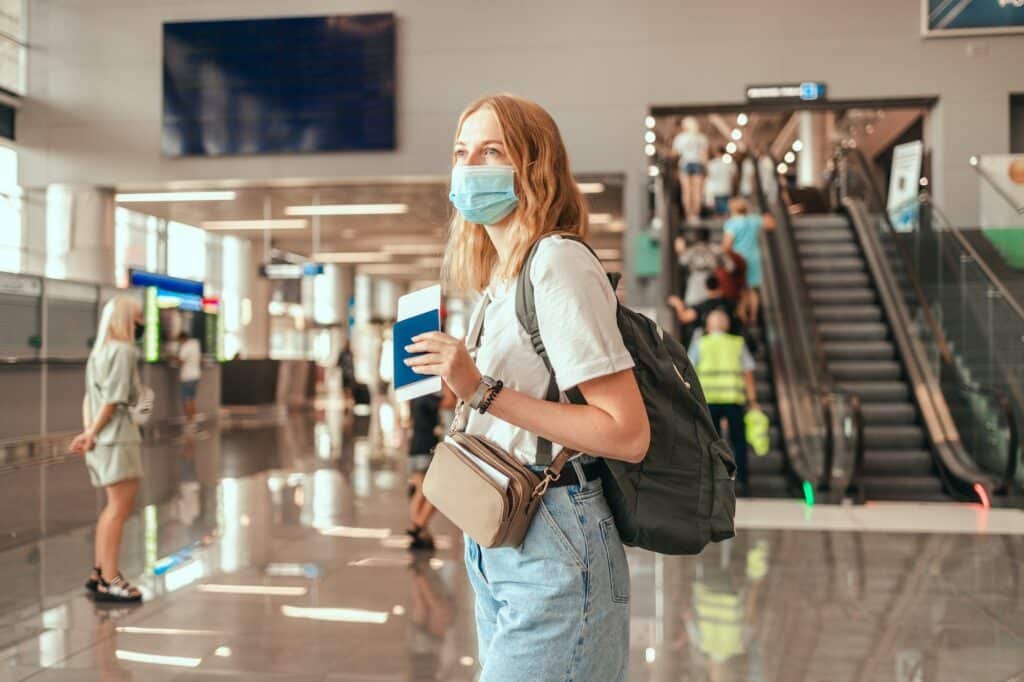 COVID-19 Young woman holding suitcase luggage with passport and plane ticket at airport for journey.