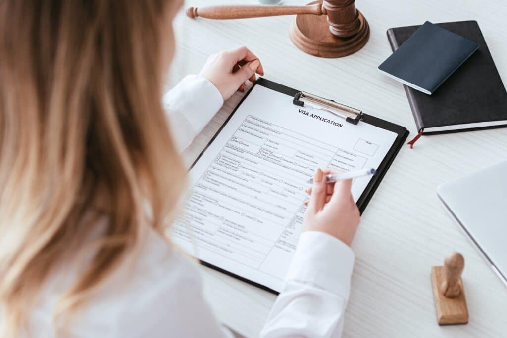 selective focus of woman holding pen near document with visa application lettering